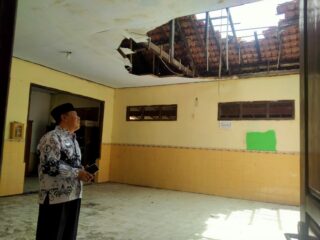 caption foto: Seorang guru meninjau kondisi ruang kelas di SDN Gunung Sekar 2 yang mengalami kerusakan parah pada bagian atap, mengancam keselamatan proses belajar-mengajar.