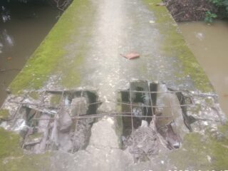 Caption Foto: Bagian lantai jembatan di Dusun Glugur, Desa Kodak, tampak berlubang besar hingga menampakkan rangka besi, memperlihatkan tingkat kerusakan parah yang setiap hari tetap dilalui warga menuju area pertanian.